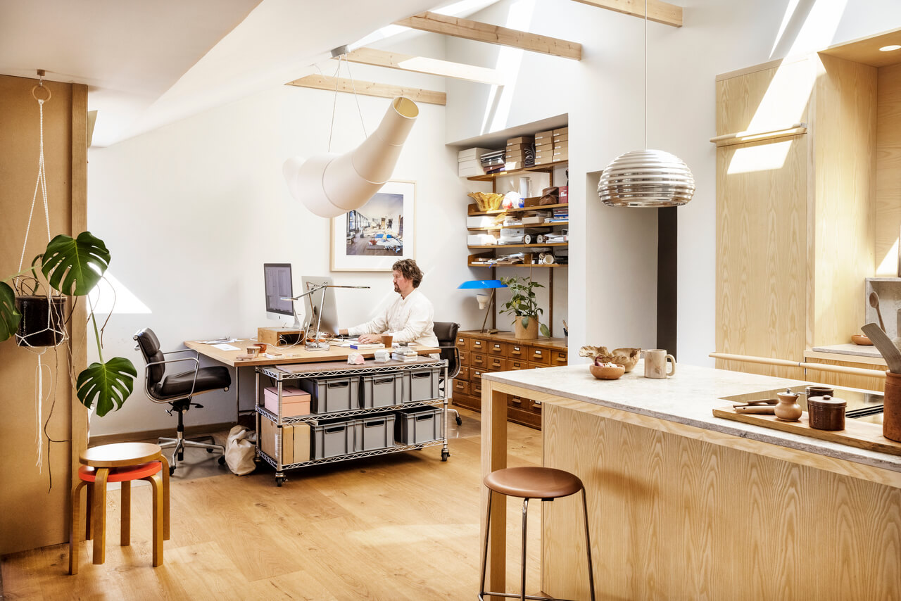 A shared dining room area together with home office. Man is sitting at the home office table and working with computer