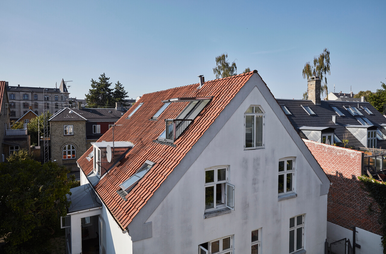 Outside view to the white painted house with red roof and roof windows.