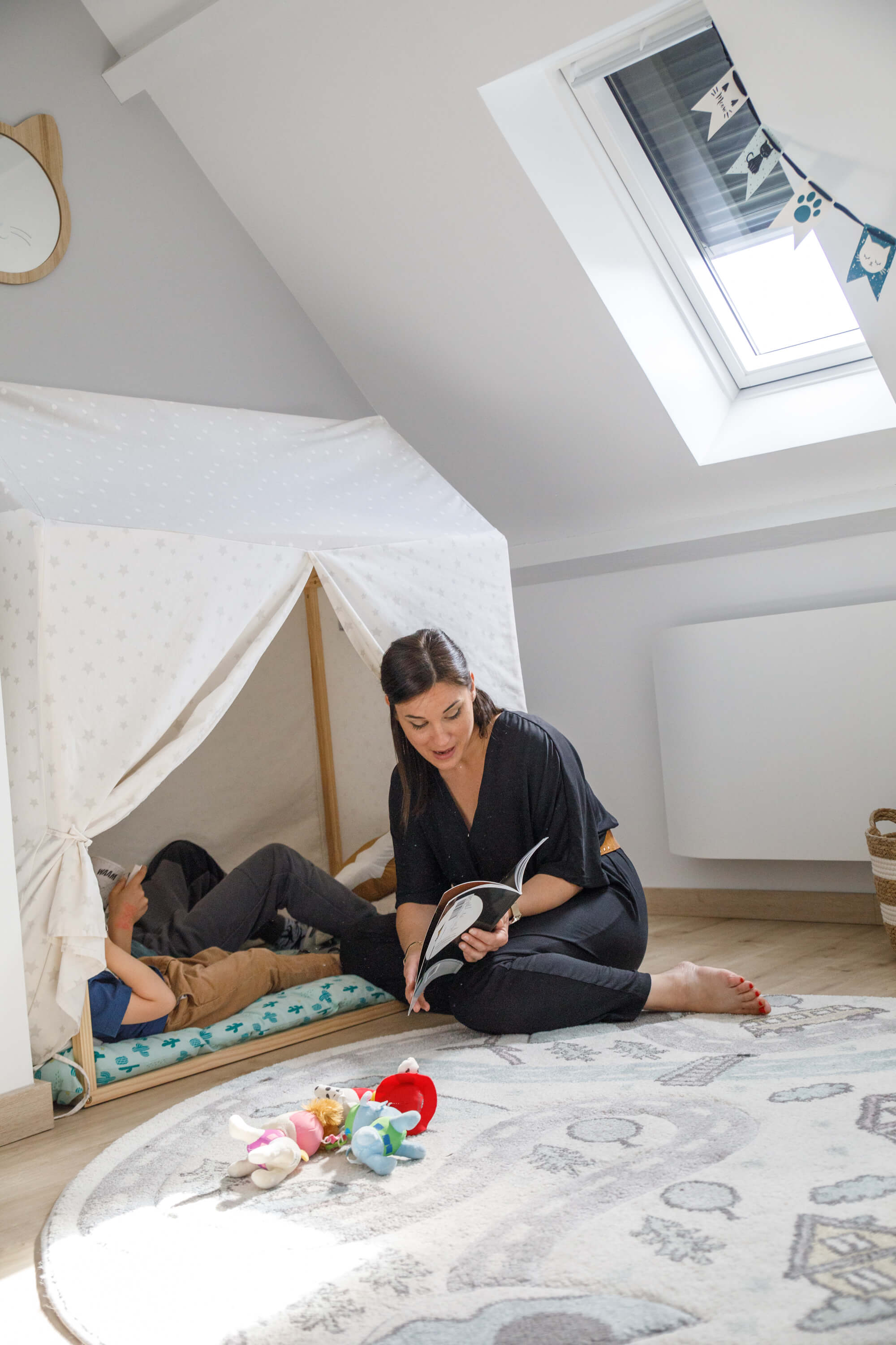 A woman reading a book for a kid, who is lying in the tent bed
