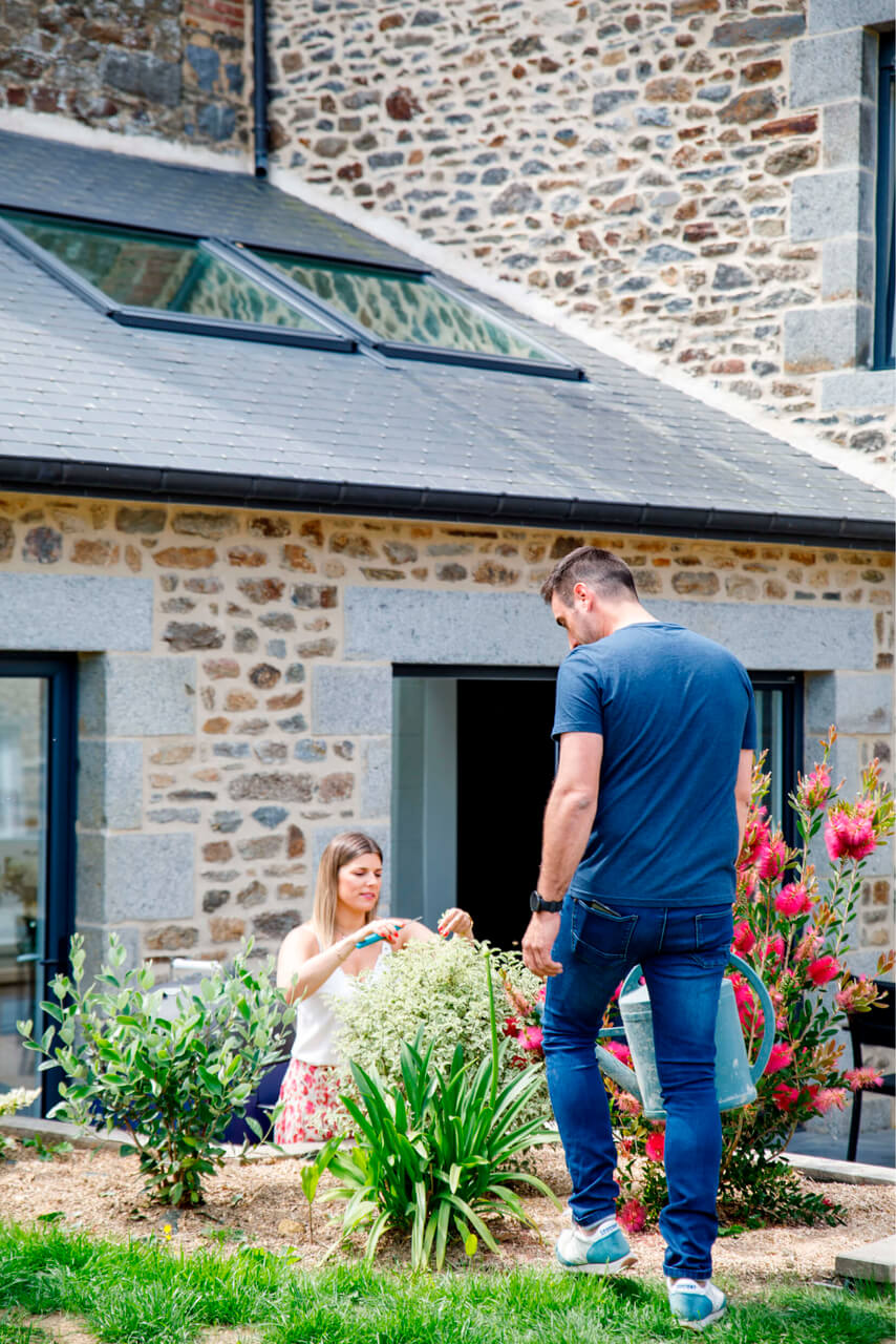 Woman working in the garden in front of the house and man is standing nearby