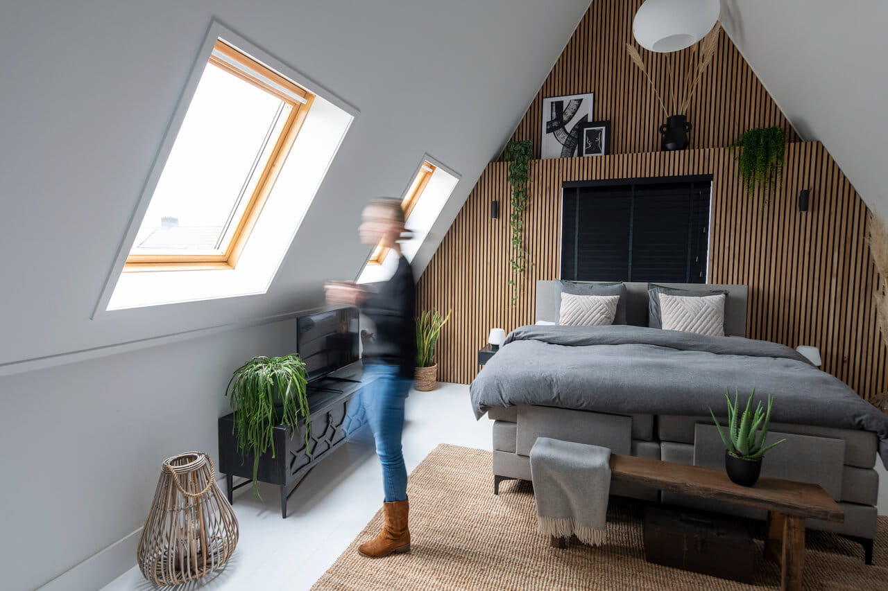 Bedroom in the attic and the woman is standing there in front of a roof window.