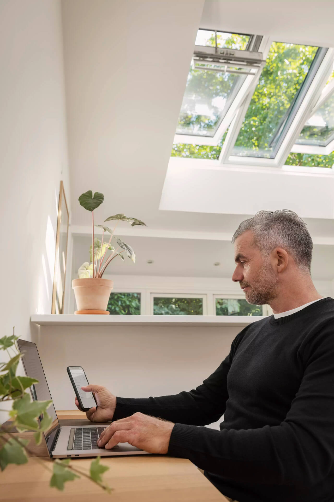 A man works on his computer while looking at his phone